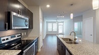 Located at 4906 Wurzbach Pkwy in San Antonio, Texas, this single-story unit offers a thoughtfully designed, contemporary interior with a cohesive aesthetic throughout. The open-concept kitchen serves as a central highlight, anchored by a large island with a double-basin sink, speckled granite countertops, and a gold-toned faucet. Dark espresso cabinetry extends to the ceiling, paired with a subway tile backsplash and a full suite of stainless steel appliances, including a refrigerator, electric range, and built-in microwave. Cylindrical pendant lights hang above the island, adding a modern touch, while recessed lighting illuminates the space. Wood-look flooring flows from the kitchen into the living area, which benefits from natural light through large windows fitted with blinds and is accented by a ceiling fan.

The bedrooms feature plush carpeting and dual windows that bring in ample natural light. A spacious walk-in closet with built-in shelving and double hanging rods provides generous storage. The primary bathroom includes a glass-enclosed shower, a separate soaking tub with white subway tile surround and a recessed niche, a dark-cabinet vanity with granite countertops, and wood-look flooring, creating a clean and functional finish throughout.