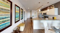 This well-appointed two-bedroom, two-bathroom residence offers a thoughtfully designed single-floor layout with a contemporary aesthetic throughout. The open-concept kitchen serves as a central hub, outfitted with stainless steel appliances including a French door refrigerator, electric range, microwave, and dishwasher. Crisp white cabinetry extends to the ceiling, complemented by a white subway tile backsplash, neutral countertops, and a large island with seating — ideal for casual dining or entertaining. Track lighting illuminates the space efficiently, while wood-style flooring flows seamlessly into the adjoining living and dining areas.

The living room features warm gray walls, a ceiling fan, and a comfortable, stylish layout. The primary bedroom is accented by a bold teal feature wall, ceiling fan, natural light from large windows, and direct access to a spacious en-suite bathroom. The primary bath includes a deep soaking tub, open shelving, white cabinetry, and tile surround. The second bedroom features a warm yellow accent wall, a ceiling fan, and a walk-in closet. The second bathroom provides a shower/tub combination with clean white finishes and wood-style flooring throughout.
