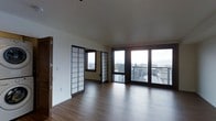 This single-floor space blends contemporary design with Japanese-inspired architectural elements, creating a distinctive and serene interior. The most striking decorative feature is the pair of traditional shoji screen sliding panels, which serve as elegant room dividers, framing a secondary area while adding a refined, minimalist aesthetic. The dark-framed shoji screens contrast tastefully with the clean white walls throughout the space.

The flooring consists of rich, warm-toned hardwood that runs continuously across the open layout, lending a sense of cohesion and spaciousness. The ceilings are smooth and generously proportioned, contributing to the overall airy quality of the interior.

Natural light is a defining characteristic, with large floor-to-ceiling windows and glass doors lining the far wall. These openings frame expansive views of the surrounding cityscape and distant mountains, flooding the interior with daylight. The glazed doors provide access to an outdoor balcony, further connecting the interior to the scenic exterior environment.

The open-plan layout offers considerable flexibility, allowing the space to be configured for a variety of uses. The overall ambiance is calm, uncluttered, and sophisticated, with a clear emphasis on natural materials and light.