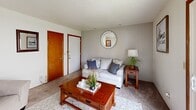 This two-bedroom, one-bathroom unit at Fountain Park in Bloomington, Indiana, offers a practical and well-organized single-floor layout. The living room features carpet flooring, a wood-paneled accent wall, and a sliding glass door that opens to an outdoor patio, allowing natural light and views of the surrounding greenery. The space accommodates a seating area and coffee table comfortably.

The kitchen is equipped with warm-toned wood cabinetry, a double stainless steel sink, laminate countertops, and white appliances including a range and refrigerator. A window brightens the adjacent dining area, which has room for a small table and seating.

The primary bedroom features carpet flooring, a window with outdoor views, and ample wall space. The second bedroom, though compact, also includes a window for natural light, a sliding wood closet door, and carpet flooring. Both rooms maintain a clean, neutral aesthetic.

The shared bathroom includes a white vanity, tile flooring, and a shower-tub combination with a curtain. Throughout the unit, warm wood door trim provides a consistent design detail, contributing to a cohesive and functional living environment.