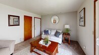 This two-bedroom, one-bathroom unit at Fountain Park in Bloomington, Indiana, offers a practical and well-organized single-floor layout. The living room features carpet flooring, a wood-paneled accent wall, and a sliding glass door that opens to an outdoor patio, allowing natural light and views of the surrounding greenery. The space accommodates a seating area and coffee table comfortably.

The kitchen is equipped with warm-toned wood cabinetry, a double stainless steel sink, laminate countertops, and white appliances including a range and refrigerator. A window brightens the adjacent dining area, which has room for a small table and seating.

The primary bedroom features carpet flooring, a window with outdoor views, and ample wall space. The second bedroom, though compact, also includes a window for natural light, a sliding wood closet door, and carpet flooring. Both rooms maintain a clean, neutral aesthetic.

The shared bathroom includes a white vanity, tile flooring, and a shower-tub combination with a curtain. Throughout the unit, warm wood door trim provides a consistent design detail, contributing to a cohesive and functional living environment.