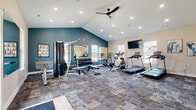 This state-of-the-art fitness center boasts a spacious, open-concept design with vaulted ceilings and ample recessed lighting, creating a bright and invigorating atmosphere. The facility is equipped with a wide array of exercise machines, including treadmills, ellipticals, stationary bikes, and weight training equipment. A dedicated free weights area includes a rack of dumbbells and benches for strength training.

The center's design incorporates a striking teal accent wall, contrasting beautifully with the neutral tones of the other walls and patterned gray carpeting. Large windows allow natural light to flood the space, while also providing views of the surrounding area. For entertainment and instruction, wall-mounted televisions are strategically placed throughout.

A notable feature is the colorful fitness accessories corner, complete with exercise balls, yoga mats, and resistance bands, adding a pop of vibrancy to the room. Mirrors line portions of the walls, allowing users to monitor their form during workouts. The space also includes a separate area for stretching and floor exercises.

The facility's layout promotes easy navigation and efficient use of space, ensuring a comfortable environment for multiple users simultaneously. With its comprehensive equipment selection and thoughtful design, this fitness center caters to a wide range of exercise preferences and fitness levels.