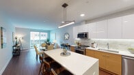 Located in the heart of Royal Oak, Michigan, this contemporary residence at 221 N Main St offers a thoughtfully designed open-concept layout that seamlessly connects the kitchen, dining, and living areas. The kitchen is a standout feature, showcasing a combination of high-gloss white upper cabinetry and warm wood-toned lower cabinets, a stone mosaic tile backsplash with under-cabinet lighting, quartz countertops, a large center island with bar seating, and a full suite of stainless steel appliances. Rich hardwood flooring flows throughout the main living areas, complementing the clean, modern aesthetic. The living room is bright and welcoming, anchored by large sliding glass doors that open to a private balcony overlooking the vibrant Royal Oak streetscape. Two well-proportioned bedrooms offer a calm retreat, featuring neutral tones and ample natural light. The bathroom is elegantly appointed with marble-look tile flooring, a floating wood vanity, and a backlit mirror, conveying a spa-like atmosphere. Throughout the space, recessed lighting and contemporary pendant fixtures provide warm, layered illumination. This single-floor residence combines modern finishes with a functional layout, making it an ideal urban living option in one of Metro Detroit's most walkable communities.