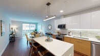 Located in the heart of Royal Oak, Michigan, this contemporary residence at 221 N Main St offers a thoughtfully designed open-concept layout that seamlessly connects the kitchen, dining, and living areas. The kitchen is a standout feature, showcasing a combination of high-gloss white upper cabinetry and warm wood-toned lower cabinets, a stone mosaic tile backsplash with under-cabinet lighting, quartz countertops, a large center island with bar seating, and a full suite of stainless steel appliances. Rich hardwood flooring flows throughout the main living areas, complementing the clean, modern aesthetic. The living room is bright and welcoming, anchored by large sliding glass doors that open to a private balcony overlooking the vibrant Royal Oak streetscape. Two well-proportioned bedrooms offer a calm retreat, featuring neutral tones and ample natural light. The bathroom is elegantly appointed with marble-look tile flooring, a floating wood vanity, and a backlit mirror, conveying a spa-like atmosphere. Throughout the space, recessed lighting and contemporary pendant fixtures provide warm, layered illumination. This single-floor residence combines modern finishes with a functional layout, making it an ideal urban living option in one of Metro Detroit's most walkable communities.