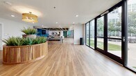 Located at 222 E Boyd in Baton Rouge, Louisiana, this 5,620 square foot single-floor amenity facility is thoughtfully designed to offer residents a diverse range of social and recreational spaces. The expansive main lounge features warm hardwood-style flooring, a distinctive coffered ceiling with dark-trimmed beams, and bold teal upholstered banquette seating alongside an eclectic mix of lounge chairs and area rugs. Floor-to-ceiling glass walls and black-framed doors flood the space with natural light while providing direct access to a landscaped outdoor courtyard with pergola and seating areas. A dedicated game room houses a full-size ping pong table and comfortable accent seating, also benefiting from large courtyard-facing windows. The private screening room offers a more intimate atmosphere, finished with charcoal walls, wood-paneled ceiling accents, acoustic wall panels, plush navy blue lounge chairs, and a large projection screen. A secondary lounge area provides a relaxed gathering space with circular sectional seating, wall-mounted TV, and decorative woven pendant lighting. Additional rooms include a flex space adorned with large-scale artwork and hardwood floors. Throughout, the design balances contemporary aesthetics with inviting, functional interiors suited for community living.
