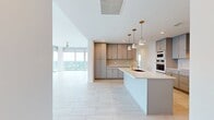 This contemporary apartment offers a generous 1730 square feet of living space, thoughtfully designed on a single floor. The heart of the home is a striking open-concept living area, showcased in the image. Floor-to-ceiling windows dominate one wall, flooding the space with natural light and providing breathtaking panoramic city views. 

The flooring throughout is a sleek, light-colored tile, enhancing the sense of spaciousness. A standout feature is the modern, gold starburst chandelier, adding a touch of elegance to the minimalist design. A structural column, seamlessly integrated into the space, subtly delineates different functional areas without interrupting the open flow.

The apartment boasts two bedrooms, including a primary bedroom of 150 square feet. With four bathrooms, the layout ensures ample privacy and convenience. Additional spaces include a hallway, four closets for storage, two laundry areas, and a combined kitchen and living room setup, perfect for entertaining. The entrance welcomes residents and guests into this sophisticated urban retreat, where modern design meets functionality in a light-filled, airy environment.