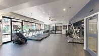 Located at 145 Commercial St in Boston's waterfront district, this fitness center offers a well-appointed, single-floor space designed to accommodate a comprehensive range of workout routines. The open floor plan is finished with durable rubber sport flooring throughout, providing a safe and functional surface for all types of exercise.

The cardio zone is lined with a row of True treadmills and additional cardio equipment, positioned alongside floor-to-ceiling windows that invite abundant natural light and offer views of the surrounding streetscape — an energizing backdrop for any workout. Large mirrors along the walls enhance the sense of space and allow for proper form checks during training.

The strength and functional training area is generously equipped with a full dumbbell rack, weight benches, medicine balls, stability balls, kettlebells, a cable machine, and a power rack. A dedicated functional training zone features a TKO heavy bag, battle ropes, and a stair climber, catering to high-intensity and cross-training workouts.

The space is climate-controlled with wall-mounted air conditioning units, and large ceiling fans contribute to air circulation throughout. Recessed lighting ensures consistent illumination across all zones. The interior design features bold navy blue accent walls contrasted with clean white ceilings, giving the facility a modern and motivating aesthetic.
