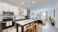 Located at 311 W 22nd St in Kansas City, MO, this thoughtfully designed one-bedroom, one-bathroom residence offers a smart and efficient single-floor layout. The open-concept living area seamlessly connects the kitchen, dining, and living spaces, creating an inviting atmosphere filled with natural light from large windows that frame urban views of the city.

The kitchen is a standout feature, boasting two-tone cabinetry with crisp white upper cabinets and slate gray lower cabinets, a classic white subway tile backsplash, stainless steel appliances, and a central island with a white quartz countertop — ideal for casual dining or meal prep. Light wood-look flooring flows throughout the main living areas, enhancing the bright, contemporary feel.

The living room offers generous space with large windows dressed in linen curtains, allowing natural light to fill the room. The bedroom features plush carpeting, a dedicated closet, and oversized windows with city views, providing a comfortable retreat. A dedicated laundry area and utility room add practical convenience.

The bathroom is cleanly finished with wood-tone flooring, a dark vanity, and a subway tile tub surround with matte black accents. Throughout the residence, the design balances modern aesthetics with functional living in the heart of Kansas City.