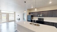 This single-story, 2-bedroom, 1-bathroom unit offers a thoughtfully designed open-concept layout with modern finishes throughout. The combined kitchen and living area forms the heart of the unit, where a large white quartz island with a stainless steel sink serves as the centerpiece. The kitchen is equipped with dark espresso cabinetry, black appliances including a refrigerator, electric range, and built-in microwave, and is illuminated by stylish pendant lights hanging above the island. Recessed lighting complements the space throughout.

The living area features durable wood-look plank flooring that extends throughout the unit, neutral-toned walls, and a glass door paired with large windows that invite natural light and provide outdoor views. Both bedrooms are well-sized, with the primary bedroom offering a ceiling fan and window with exterior views. The second bedroom maintains the same clean, neutral aesthetic.

The bathroom includes a dark-cabinetry vanity with a white countertop, a large mirror, and contemporary lighting fixtures. Two walk-in closets are outfitted with multi-tiered wire shelving and hanging systems, providing generous and organized storage throughout the unit.