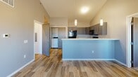 Located at 2300 N Valley View Rd in Sioux Falls, South Dakota, this well-designed 2-bedroom, 2-bathroom unit offers a thoughtful single-floor layout that maximizes both function and comfort. The open-concept living and kitchen area immediately impresses with soaring vaulted ceilings and warm wood-style plank flooring throughout. The kitchen is outfitted with grey shaker-style cabinetry, light quartz countertops, black appliances including a range, microwave, and refrigerator, and a peninsula with pendant lighting that provides additional prep and dining space. An adjacent utility room conveniently houses in-unit laundry. Both bedrooms are carpeted and receive natural light through window blinds, offering a cozy, quiet retreat. The spacious primary bedroom includes its own dedicated closet, while a second walk-in closet provides generous additional storage with built-in shelving. Each of the two bathrooms features wood-style tile flooring, a tub/shower combination with a curved curtain rod, and grey vanity cabinetry with quartz countertops. A connecting hallway with modern wood-grain doors ties the layout together. The overall aesthetic is clean and contemporary, with a neutral grey and white palette that creates a bright, cohesive atmosphere throughout.