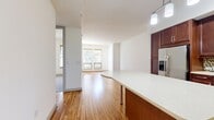 This 660-square-foot, one-bedroom, one-bathroom apartment is located at Griffis Uptown in Dallas, TX. The open-concept kitchen and living area serves as the heart of the unit, showcasing warm-toned hardwood flooring throughout. The well-appointed kitchen features rich dark wood cabinetry, stainless steel appliances including a refrigerator with ice maker, dishwasher, microwave, and range, complemented by a mosaic tile backsplash and a central island with a light quartz countertop — ideal for dining or meal prep. The living area is bright and airy, with built-in shelving, a glass-paneled exterior door that invites natural light, and a ceiling fan overhead. The 130-square-foot primary bedroom is carpeted for comfort, featuring two windows with tree-lined views and a ceiling fan. A dedicated closet provides additional storage. The full bathroom is finished with large-format tile flooring, a soaking tub with stone-tiled surround, and a rich wood vanity with ample cabinet storage and a mirror. The unit combines upscale finishes with a functional layout in one of Dallas's most vibrant urban neighborhoods.