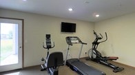 This single-floor fitness room offers a straightforward and functional workout environment designed to meet essential exercise needs. The space features a carpeted floor and neutral-toned walls that create a clean, no-frills atmosphere conducive to focused exercise sessions. Recessed ceiling lighting provides consistent, even illumination throughout the room.

The fitness area is equipped with three key cardio machines: a stationary upright exercise bike, a motorized treadmill, and an elliptical cross-trainer, each positioned to allow comfortable use without feeling cramped. Each machine features its own digital display console, enabling users to monitor workout metrics such as speed, distance, and time.

A flat-screen television is mounted on the wall at an optimal viewing height, allowing users to watch programming while exercising. The overall layout is efficient, making practical use of the available space. The room's design prioritizes utility, with its simple décor and dedicated equipment arrangement making it a practical amenity for those seeking a convenient on-site fitness option.