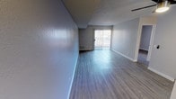 This single-floor unit offers a thoughtfully arranged layout with updated finishes throughout. The main living area features wood-look laminate flooring in a cool gray tone, neutral-painted walls, and a textured ceiling. A ceiling fan provides added comfort, while a sliding glass door fitted with vertical blinds floods the space with natural light and provides access to an outdoor area.

The galley-style kitchen is efficiently designed with white cabinetry, gray quartz-style countertops, a stainless steel double sink, and black appliances including a refrigerator and range. Ample upper and lower cabinet storage lines both walls, and a window with vertical blinds allows natural light into the space.

The bedroom features wood-look flooring, neutral gray walls, a textured ceiling, and a wide mirrored sliding closet that enhances the sense of space. A barred window provides natural light and views of the surrounding area.

The bathroom is clean and functional, featuring a white tub-shower combination with a curved curtain rod and brushed nickel fixtures, a vanity with a light stone-style countertop, and wood-look flooring. The overall ambiance of the unit is clean, modern, and move-in ready.