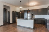 Located at 1700 Broad St in Chattanooga, Tennessee, this single-floor residence offers a contemporary and well-appointed living experience. The open-concept kitchen serves as a central highlight, featuring dark espresso cabinetry, dark granite countertops, a large center island with a built-in sink, subway tile backsplash, and stainless steel appliances including a range, microwave, and refrigerator. Stylish pendant lighting hangs above the island, adding a modern touch. Rich hardwood-style flooring flows throughout the main living and kitchen areas, creating a warm and cohesive aesthetic. The spacious living room is anchored by French doors that open to a private balcony, offering outdoor views and abundant natural light. A built-in wall niche provides an architectural accent. The bedrooms are comfortably carpeted and feature ceiling fans and windows with blinds that allow for natural light. The bathrooms are finished with dark cabinetry, granite vanity tops, wood-look flooring, and tiled tub-shower combinations. The overall design balances modern finishes with a neutral palette, creating a clean, inviting atmosphere throughout the unit.