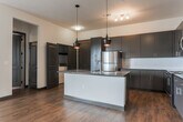 Located at 1700 Broad St in Chattanooga, Tennessee, this single-floor residence offers a contemporary and well-appointed living experience. The open-concept kitchen serves as a central highlight, featuring dark espresso cabinetry, dark granite countertops, a large center island with a built-in sink, subway tile backsplash, and stainless steel appliances including a range, microwave, and refrigerator. Stylish pendant lighting hangs above the island, adding a modern touch. Rich hardwood-style flooring flows throughout the main living and kitchen areas, creating a warm and cohesive aesthetic. The spacious living room is anchored by French doors that open to a private balcony, offering outdoor views and abundant natural light. A built-in wall niche provides an architectural accent. The bedrooms are comfortably carpeted and feature ceiling fans and windows with blinds that allow for natural light. The bathrooms are finished with dark cabinetry, granite vanity tops, wood-look flooring, and tiled tub-shower combinations. The overall design balances modern finishes with a neutral palette, creating a clean, inviting atmosphere throughout the unit.