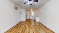 Located at 1006 N El Centro Ave in Hollywood, Los Angeles, this efficiently designed studio unit makes smart use of its single-floor layout. The open-plan living and kitchen area forms the heart of the space, finished with warm, light-toned hardwood-style flooring that runs throughout and crisp white walls that keep the interior feeling bright and airy. A ceiling fan with integrated lighting anchors the living area, while a wall-mounted HVAC unit ensures year-round comfort. A set of glass-paneled French doors floods the room with natural light and provides access to the outdoors. The kitchen runs along one wall and is outfitted with white cabinetry, a tile backsplash, a single-basin sink, a freestanding range, a range hood, and a full-size refrigerator — providing all essential cooking amenities in a clean, functional arrangement. A dedicated closet offers convenient storage. The bathroom features full white subway tile surround walls and a walk-in shower with penny-tile flooring and chrome fixtures, maintaining the unit's clean, all-white aesthetic. Textured ceilings add a subtle design detail throughout. The overall ambiance is clean, minimal, and move-in ready, well-suited for those seeking a practical residence in the heart of Hollywood.