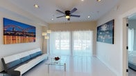 The Ramona is a well-appointed 1-bedroom, 1-bathroom residence that combines modern design with a clean, bright aesthetic throughout its single-floor layout. The living area serves as the heart of the unit, featuring gleaming white tile flooring, a ceiling fan with integrated lighting, and recessed ceiling lights that complement the natural light streaming through large sliding glass doors dressed in sheer white curtains. The open feel is enhanced by cityscape artwork adorning the walls, adding a vibrant touch to the neutral palette.

The kitchen is thoughtfully designed with white shaker-style cabinetry, granite countertops, stainless steel appliances including a French door refrigerator and electric range, and a dishwasher. Wall-mounted pot racks provide practical storage, while the white tile flooring and bright cabinetry maintain a cohesive, clean look throughout.

The bedroom offers plush carpeting, a sliding glass door with sheer curtains for natural light and outdoor access, and ample closet space accessible through paneled double doors. The neutral tones create a calm, restful environment.

The bathroom features wood-look tile flooring, a white vanity with a clean-lined mirror, and a modern paneled door, maintaining the unit's consistent contemporary style. Overall, The Ramona presents a bright, modern living experience.
