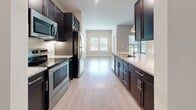 Located at 13504 Citicards Way in Jacksonville, FL, this well-appointed 870-square-foot, one-bedroom, one-bathroom apartment offers a thoughtfully designed single-floor layout. The open-concept kitchen and living area serves as the heart of the unit, featuring light wood-tone flooring, recessed lighting, and pendant lights over a granite-topped kitchen island with a built-in sink. Dark espresso cabinetry, including a built-in wine rack, contrasts elegantly with the light granite countertops and tile backsplash. Stainless steel appliances, including a refrigerator, range, and microwave, complete the modern kitchen. The spacious living area flows naturally from the kitchen, bathed in natural light from large windows and equipped with a ceiling fan. The 150-square-foot primary bedroom features plush carpeting, a ceiling fan, dual windows with outdoor views, and direct access to a closet. The bathroom includes light wood-tone flooring, a tub/shower combination, and stylish two-panel doors. A dedicated laundry room houses a full-size top-load washer with overhead shelving and hardwood-style flooring. Neutral warm-toned walls throughout lend a clean, modern ambiance to the entire unit.