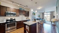 This single-floor residence is designed with an open-concept layout that seamlessly connects the kitchen, dining, and living areas. The kitchen is a standout feature, outfitted with rich dark wood cabinetry, a classic white subway tile backsplash, stainless steel appliances, granite countertops, and a central island with bar seating. Track lighting and pendant lights illuminate the space effectively, while wood-look flooring adds warmth throughout.

The living area is bright and inviting, anchored by a ceiling fan and a large sliding glass door that opens to a private balcony, offering views of the surrounding neighborhood. Natural light flows generously through floor-to-ceiling windows.

The bedroom continues the comfortable aesthetic with plush carpeting, its own sliding glass balcony door, and access to a spacious walk-in closet featuring wrap-around wire shelving systems for organized storage.

The bathroom is finished with tile flooring, a dark wood vanity with a clean white countertop, and a full tub-shower combination accented by classic white and grey tile surround. The overall design balances modern functionality with a warm, livable ambiance throughout.