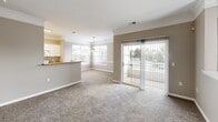 This two-story home in Fort Wayne, Indiana offers a thoughtfully designed layout across two floors, with the main living areas comprising the bulk of the space. The open-plan main floor features a combined dining and living room with plush carpeting, crown molding, and a sliding glass door that opens onto a private balcony with outdoor views. The kitchen is well-appointed with white cabinetry, granite-style laminate countertops, a breakfast bar peninsula, white appliances including a refrigerator and range, and light wood-look flooring that carries through the space. Both bathrooms are finished with white vanities, granite-style countertops, and light wood-look flooring; one features a walk-in shower and the other a full tub-shower combo. The two bedrooms are carpeted and bright, each with natural light from windows and access to closets—five closets are distributed throughout the home, providing generous storage. The spacious primary bedroom includes a ceiling fan and a dedicated closet. Carpeted staircases with white railings connect the floors, and a utility room provides additional functionality. Neutral warm-gray tones throughout create a cohesive and welcoming ambiance.
