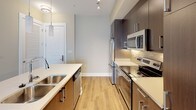 This single-floor residence offers a thoughtfully designed layout with contemporary finishes and a cohesive neutral color palette throughout. The kitchen is a standout feature, showcasing dark espresso cabinetry with sleek hardware, light quartz countertops, a tile backsplash, and a full suite of stainless steel appliances including a refrigerator, range, and over-the-range microwave. A double-basin sink with pendant lighting and a breakfast bar add both functionality and style, while light hardwood-style flooring ties the space together. The open living and dining area extends naturally from the kitchen, featuring the same warm hardwood-style flooring and neutral warm-toned walls that create a bright, welcoming atmosphere. French doors in the living area invite natural light and provide access to an outdoor space. The bedroom is finished with plush carpeting and features dual windows with blinds that allow for ample natural light. The full bathroom is clean and well-appointed, with light tile flooring, a dark vanity with quartz countertop, and a tiled shower-tub combination. A dedicated hallway with closet access adds practical storage. Overall, the space presents a modern and functional design with consistent, quality finishes throughout.