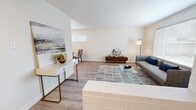 This thoughtfully designed 2-bedroom, 2-bathroom single-floor residence offers a cohesive mid-century modern aesthetic throughout. The combined living and dining area serves as the heart of the home, characterized by painted white brick accent walls, light hardwood-style flooring, and generous natural light streaming through large windows with blinds. The living space comfortably accommodates a seating area alongside a dedicated dining nook with a round glass-top table.

The galley-style kitchen is efficiently laid out, featuring white shaker cabinetry, dark countertops, and a full suite of stainless steel appliances including a refrigerator, range, and dishwasher. A hallway connects the main living areas to the private quarters.

The primary bedroom is a well-proportioned retreat with a painted brick accent wall, a window with exterior views, a closet with louvered doors, and light wood flooring. The second bedroom features smooth walls, dual bedside lamps, and a calm, restful ambiance.

Both bathrooms are updated with white vanity cabinetry, dark stone countertops, under-mount sinks, chrome fixtures, and mirrored medicine cabinets. Light wood flooring continues consistently throughout the unit, reinforcing the home's clean, modern character.