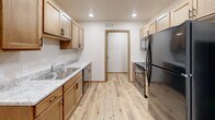This single-floor unit offers a thoughtfully organized layout across seven rooms, making efficient use of its intimate footprint. The kitchen is a functional highlight, featuring warm honey-toned cabinetry with matte black hardware, light granite-style countertops, a stainless steel sink, and a full suite of stainless steel appliances including a refrigerator, range, microwave, and dishwasher. Light-toned luxury vinyl plank flooring runs throughout the kitchen and main living areas, lending a clean and cohesive aesthetic. The living area is carpeted and brightened by a sliding glass door dressed with vertical blinds, allowing natural light to filter in. The bedroom is similarly carpeted and features a window with blinds, along with dual closets providing ample storage. An additional room offers flexible use as a second bedroom or office. The full bathroom is finished with a wood-trimmed vanity, granite-style countertop, matte black fixtures, a wall-mounted mirror cabinet, and a tub-shower combination. Neutral walls, consistent wood-trimmed door frames, and recessed lighting throughout tie the space together with a clean, move-in-ready presentation.