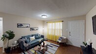 This single-story residence offers a thoughtfully arranged floor plan with distinct living, dining, kitchen, bedroom, and bathroom areas. The living room serves as the heart of the home, featuring warm hardwood-style flooring, a textured ceiling, and a front-facing window dressed with vibrant yellow sheer curtains that bathe the space in natural light. A flush-mount ceiling light provides additional illumination, and the room comfortably accommodates a full seating arrangement with a sofa, accent chair, and coffee table.

The kitchen is well-equipped, showcasing rich dark cabinetry paired with granite-style countertops and stainless steel appliances, including a range and over-the-range microwave. A double-basin sink sits beneath a window, enhancing the workspace's functionality.

The two bedrooms are carpeted for comfort, each featuring a ceiling fan or dedicated lighting, closet space, and windows for natural light. The rooms offer a calm, restful atmosphere suitable for relaxation.

Both bathrooms are efficiently laid out, each with a vanity featuring a dark cabinet base and white countertop, a tub-shower combination, and tasteful décor accents that contribute to a clean, cohesive aesthetic throughout the home.