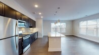 This single-floor residence is designed with a contemporary, functional layout that balances open communal spaces with private rooms. The kitchen serves as a central highlight, outfitted with rich dark cabinetry extending to the ceiling, stainless steel appliances including a gas range, microwave, dishwasher, and refrigerator, granite countertops, and a subtle tile backsplash. A central island with a matching granite surface provides additional workspace and seating, illuminated overhead by pendant lighting. The kitchen flows directly into the living and dining area, which is finished with durable hardwood-style flooring and receives natural light through large windows fitted with horizontal blinds.

The bedrooms feature neutral-toned carpet flooring and windows that bring in natural daylight. Two bathrooms serve the unit: one features a subway-tiled shower-tub combination with a dark vanity and granite countertop, while the other offers a glass-enclosed subway-tiled walk-in shower with a matching vanity. Both bathrooms are finished with light tile flooring. A dedicated laundry area is also present within the unit. Hallways feature white panel doors with brushed nickel hardware, contributing to the clean, cohesive aesthetic throughout.