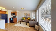 This thoughtfully designed one-bedroom, one-bathroom residence delivers a comfortable and practical single-floor living experience. The open-concept living area is bright and welcoming, featuring light wood-style flooring throughout, neutral walls, and multiple windows fitted with horizontal blinds that allow for excellent natural light and outdoor views of the surrounding community. The living room offers generous seating space and flows naturally into a dedicated sitting nook lined with additional windows on two sides, creating an airy, light-filled corner ideal for relaxing.

The kitchen is well-equipped with warm wood cabinetry, granite countertops, black appliances including a refrigerator, range, and microwave, and a peninsula that provides additional prep and casual dining space. A dedicated laundry area with a stacked washer and dryer is conveniently located just off the kitchen.

The bedroom is a calm retreat featuring a ceiling fan, natural light from a window, and a spacious walk-in closet outfitted with wire shelving and hanging rods for organized storage. A dedicated desk nook within the bedroom provides a functional workspace.

The bathroom features a wide granite-topped vanity with warm wood cabinetry, a large mirror, and clean, neutral finishes that complete the cohesive aesthetic of the home.