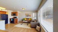 This thoughtfully designed one-bedroom, one-bathroom residence delivers a comfortable and practical single-floor living experience. The open-concept living area is bright and welcoming, featuring light wood-style flooring throughout, neutral walls, and multiple windows fitted with horizontal blinds that allow for excellent natural light and outdoor views of the surrounding community. The living room offers generous seating space and flows naturally into a dedicated sitting nook lined with additional windows on two sides, creating an airy, light-filled corner ideal for relaxing.

The kitchen is well-equipped with warm wood cabinetry, granite countertops, black appliances including a refrigerator, range, and microwave, and a peninsula that provides additional prep and casual dining space. A dedicated laundry area with a stacked washer and dryer is conveniently located just off the kitchen.

The bedroom is a calm retreat featuring a ceiling fan, natural light from a window, and a spacious walk-in closet outfitted with wire shelving and hanging rods for organized storage. A dedicated desk nook within the bedroom provides a functional workspace.

The bathroom features a wide granite-topped vanity with warm wood cabinetry, a large mirror, and clean, neutral finishes that complete the cohesive aesthetic of the home.