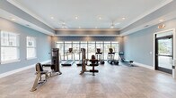 Located at 1005 Sonoran Cir in Summerville, SC, this fitness center offers a well-appointed, single-floor workout facility designed to accommodate a comprehensive range of exercise needs. The space is finished with soft blue-gray walls, crown molding, and neutral toned flooring, creating a clean and inviting atmosphere throughout.

A floor-to-ceiling window wall along one side of the room floods the interior with natural light while providing views of the surrounding community. Recessed lighting and dual ceiling fans ensure the space remains bright and comfortable during any workout. Large mirrors are strategically placed to enhance the sense of openness and assist with proper form during training.

The fitness center is outfitted with a solid selection of cardio equipment, including multiple treadmills, elliptical trainers, and a rowing machine. Strength training is well represented with a variety of cable machines, weight benches, and a free weight rack stocked with dumbbells. The open layout allows for easy movement between stations without feeling crowded.

Double glass French doors connect the fitness center to an adjacent amenity space, contributing to an integrated community feel. The overall design balances functionality with aesthetic appeal, making this a polished and practical facility for residents of the Summerville community.