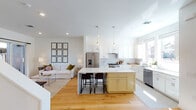 This well-designed two-floor home offers a thoughtful layout with modern finishes and a bright, airy atmosphere throughout. The open-concept main living area seamlessly connects the kitchen and living room, anchored by light hardwood flooring that flows throughout the space. The kitchen is a standout feature, boasting crisp white shaker cabinetry, a classic subway tile backsplash, stainless steel appliances, and a central island with a contrasting soft yellow base and white quartz countertop — complete with bar seating and pendant lighting overhead. The adjacent living area provides direct outdoor access through a sliding glass door leading to a private balcony or patio. A dedicated dining area accommodates a full dining set beneath a striking pendant light, complemented by bold artwork. The bedrooms are generously proportioned, bathed in natural light from large windows, and feature ceiling fans and hardwood floors. The primary bathroom is a luxurious retreat with a double-sink vanity, marble-veined accent wall, walk-in tile shower, hexagonal tile flooring, and an adjoining walk-in closet. A secondary bathroom features charming blue floral wallpaper, hexagonal tile floors, a soaking tub, and classic white cabinetry. An additional flexible room offers versatile living space, ideal as a lounge, playroom, or home office.