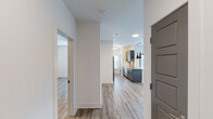 This well-appointed single-floor residence offers a thoughtfully designed open-concept layout that seamlessly connects the kitchen and living area. Light wood-tone flooring runs consistently throughout, lending a clean, cohesive aesthetic to every room. The kitchen is a standout feature, showcasing dark cabinetry with matte black hardware, granite countertops, a tile backsplash, and a full suite of stainless steel appliances including a range, microwave, and refrigerator. A peninsula with pendant lighting provides additional prep space and serves as a natural divider between the kitchen and the expansive living area, which is bathed in natural light from multiple windows and topped with a ceiling fan. A dedicated entry hall with panel-style gray doors provides a welcoming transition into the home. The bedrooms are generously sized, each with continued wood-tone flooring and ceiling fans. Two bathrooms serve the residence: one features a soaking tub with marble-style tile surround and granite vanity, while the second offers a glass-enclosed walk-in shower with matching marble-style tile. A dedicated laundry room with a full-size washer and dryer adds everyday convenience. The overall ambiance is modern, bright, and move-in ready.
