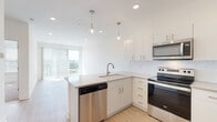 Located at 110 W Hillsdale St in Lansing, Michigan, this single-floor residence offers a thoughtfully designed layout with modern finishes throughout. The open-concept kitchen is a standout feature, showcasing white shaker-style cabinetry, a white subway tile backsplash, quartz countertops, and a suite of stainless steel Whirlpool appliances including a refrigerator, electric range, microwave, and dishwasher. Pendant lighting above the peninsula adds a contemporary touch, while light wood-style flooring flows through the main living areas. Natural light pours in through large windows and a sliding glass door that offers views of the surrounding neighborhood. A dedicated in-unit laundry area with a stacked washer and dryer provides everyday convenience. The bedroom features plush carpeting and a generously sized window with city views. The bathroom is finished with a wide vanity, quartz countertop, white cabinetry with brushed hardware, a large mirror, and a combination tub and shower. The overall aesthetic is clean, bright, and contemporary, creating a welcoming and functional living environment in the heart of downtown Lansing.