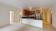 This single-floor residence offers a thoughtfully designed open-concept layout that seamlessly connects the kitchen and living area. The kitchen is a functional highlight, featuring warm medium-toned wood cabinetry, dark granite countertops, stainless steel appliances including a gas range, over-the-range microwave, and refrigerator, as well as a peninsula that defines the space and provides additional prep area. Track lighting above the kitchen adds focused illumination, while recessed lighting brightens the adjoining living area. The living space features plush wall-to-wall carpeting and large sliding glass doors and windows that invite natural light and urban views. Two generously sized bedrooms continue the carpeted flooring and neutral palette, each offering ample space and natural light through large windows overlooking the surrounding streetscape. One bedroom includes access to a spacious walk-in closet fitted with wire shelving for versatile storage. The two bathrooms are finished with granite-topped wood vanities, chrome fixtures, and neutral tile flooring, offering a clean and cohesive aesthetic. Throughout the residence, a consistent use of warm wood tones, soft neutrals, and quality finishes creates a comfortable and polished living environment.