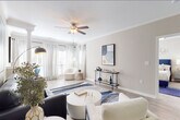 This single-floor residence offers a cohesive, contemporary design highlighted by light wood-look flooring, neutral warm-toned walls, and abundant natural light throughout. A welcoming entry hallway leads into the main living areas, where the open-concept living room impresses with crown molding, a ceiling fan, and large windows dressed in elegant striped drapes that flood the space with daylight. The living room features a dedicated reading nook anchored by a plush accent chair and additional windows with plantation shutters, creating a bright and inviting retreat.

The kitchen is well-equipped with white shaker-style cabinetry, white quartz countertops, a subway tile backsplash, and stainless steel appliances including a range, microwave, and dishwasher. A peninsula counter connects seamlessly to the dining area, which features crown molding and space for a round dining table. The bedroom is generously sized with a ceiling fan, carpeted flooring, ample natural light from a window with blinds, and access to a closet. The bathroom includes a soaking tub and shower combo, a white vanity with quartz countertops, and wood-look tile flooring. Throughout, the design maintains a clean, modern aesthetic with consistent finishes and tasteful detailing.