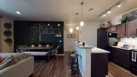 Located in Tucson, Arizona, this single-floor residence offers a thoughtfully designed open-concept layout with rich wood-look flooring flowing throughout the main living areas. The kitchen is a standout feature, equipped with dark espresso cabinetry, black appliances, granite countertops, and a peninsula breakfast bar with pendant lighting overhead — ideal for both casual dining and meal preparation. Adjacent to the kitchen, the dining area is distinguished by a bold chalkboard accent wall that adds a creative, personalized touch to the space. The living room is warm and inviting, featuring recessed lighting, a ceiling fan, and sliding glass doors that open onto a private balcony with outdoor views. The two bedrooms are carpeted for comfort, each with large windows fitted with blinds and drape panels that allow for natural light control. The full bathroom features a tub-shower combination with tile surround, wood-look flooring, and open shelving for storage. Throughout the residence, the design balances modern finishes with practical functionality, creating a cohesive and comfortable living environment well-suited to everyday life in the Sonoran Desert climate.