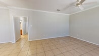 This single-story home in Cleburne, Texas offers a well-organized layout featuring two bedrooms, two bathrooms, a combined kitchen and living area, a dedicated hallway, and two closets. The living room is a generously sized, open space finished with light neutral walls, crown molding, and large-format tile flooring that extends throughout the main areas. A ceiling fan overhead and large windows with blinds allow natural light to fill the room, creating a bright and airy atmosphere. The kitchen is equipped with rich, warm-toned raised-panel wood cabinetry that extends to the ceiling for ample storage, a dishwasher, an electric range, and light countertops, all complemented by matching tile flooring and crown molding details. Both bedrooms are carpeted and feature ceiling fans and natural light from windows. The primary bedroom offers a comfortable, well-proportioned space with its own closet. The two bathrooms are finished with tile flooring, wood vanity cabinetry, white countertops, and large mirrors. One bathroom includes accessibility grab bars for added convenience. Throughout the home, a consistent neutral color palette, clean lines, and practical finishes create a cohesive and comfortable living environment.