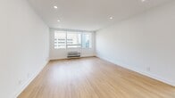 This thoughtfully designed 1-bedroom, 1-bathroom unit offers a clean, modern aesthetic throughout its efficiently laid-out single floor. Light wood flooring flows consistently across all living areas, complementing the crisp white walls and creating a bright, airy atmosphere.

The open living area is illuminated by recessed lighting and features large windows that frame expansive city skyline views, flooding the space with natural light. A wall-mounted HVAC unit provides convenient climate control directly within the living space.

The kitchen is a functional and stylish highlight, featuring light wood cabinetry with matte black hardware, marble-look countertops, stainless steel appliances including a full-size refrigerator, and a black-accented sink. A wide window above the counter offers sweeping urban views, making the kitchen as scenic as it is practical.

The bedroom is a well-proportioned retreat with large windows overlooking the city skyline, light wood flooring, and a wall-unit HVAC system, ensuring a comfortable and bright environment.

The bathroom showcases refined finishes, including floor-to-ceiling marble-look tile in the walk-in shower, a frameless glass enclosure, matte black fixtures and hardware, a built-in niche, and a rain showerhead — delivering a spa-like experience in a compact, elegant space.