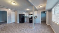 This single-floor, two-bedroom, one-bathroom unit offers a practical and cohesive design throughout. The open-concept living and kitchen area is unified by light-toned vinyl plank flooring and cool gray walls, creating a clean, neutral aesthetic. A structural support column defines the transition between the living space and the kitchen without fully enclosing either area. Natural light enters through blinded windows, brightening the main living zone, which also features a dedicated entry door.

The kitchen is efficiently designed with white shaker-style cabinetry, granite-look countertops, a double-basin stainless steel sink, and black appliances including a refrigerator, electric range with overhead ventilation, and oven. Upper and lower cabinet storage provides ample functionality.

Both bedrooms feature darker vinyl plank flooring, gray-toned walls, and closets with bifold doors for organized storage. One bedroom includes a ceiling fan and a window for natural light, while the other offers a similarly sized, quiet layout.

The bathroom is finished with a white vanity topped with granite-look counters, wood-look vinyl flooring, and a tiled tub-shower combination with dark earth-toned tile surround, complemented by a window above for ventilation.