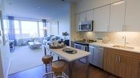 This well-appointed single-floor residence offers a thoughtfully designed open-concept layout that seamlessly connects the kitchen, dining, and living areas. The kitchen is outfitted with stainless steel appliances, including a built-in microwave, gas range, and dishwasher, complemented by crisp white cabinetry, a mosaic tile backsplash, and light quartz countertops. Warm wood-toned lower cabinets add a contemporary contrast to the overall design. A central kitchen island with bar-height seating provides a casual spot for dining or entertaining. Rich hardwood flooring flows throughout, grounding the space with warmth and continuity. The adjacent living area is bathed in natural light from large windows that frame views of the surrounding landscape, creating an airy and inviting atmosphere. Neutral tones throughout the interior are accented by tasteful décor, contributing to the space's modern yet comfortable character. Recessed lighting enhances the clean architectural lines, while the open floor plan promotes an effortless sense of flow from one area to the next.