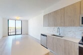 Located at 4465 Griffin Rd in Hollywood, FL, this well-appointed one-bedroom, one-bathroom unit offers a thoughtfully designed open-concept layout that seamlessly connects the kitchen, dining, and living areas. Light wood-tone flooring flows throughout, complementing the clean white walls and creating a bright, airy ambiance. The modern kitchen is a standout feature, showcasing flat-panel wood cabinetry, a white quartz waterfall island, stainless steel appliances including a refrigerator with ice maker, dishwasher, range, and microwave, along with a textured tile backsplash and undermount sink. Floor-to-ceiling sliding glass doors flood the living and bedroom areas with abundant natural light and open to a private balcony offering open outdoor views. The bedroom is a comfortable retreat, benefiting from the same light flooring, large windows, and direct balcony access. Three closets provide generous storage throughout the unit. The bathroom is finished with large-format marble-style tile surrounding a soaking tub and shower combo. Additional conveniences include an in-unit laundry area, a dedicated entrance, and a hallway connecting all spaces efficiently. The overall design aesthetic is clean, contemporary, and functional.