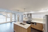 Located in the established SW Calgary neighbourhood of Elbow Drive, this thoughtfully designed two-storey home offers 2 bedrooms, 3 bathrooms, and a functional layout spread across two well-proportioned floors. The main floor centres around an open-concept kitchen and living area finished with rich dark hardwood flooring throughout. The kitchen is a standout feature, showcasing warm wood cabinetry paired with crisp white upper cabinets, light stone countertops with a central island and undermount sink, a tile backsplash, stainless steel appliances including a French door refrigerator and range, and stylish pendant lighting. Recessed pot lights illuminate the living area, which benefits from large windows that invite natural light. Carpeted staircases with white balustrades connect the two levels. Upstairs, both bedrooms offer generous proportions and direct access to private balconies through large sliding glass doors, framing pleasant neighbourhood views. The primary bedroom features a bold geometric accent wall and a well-appointed walk-in closet with built-in shelving and hanging rods. The three bathrooms are finished with marble-style countertops, white cabinetry, and light tile flooring. A dedicated in-unit laundry room with stacked washer and dryer adds everyday convenience, complemented by additional utility and storage spaces throughout.