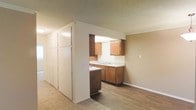 This single-floor residence offers a practical and functional layout designed to maximize everyday living. The kitchen is a central feature of the space, outfitted with warm wood-toned cabinetry that provides generous upper and lower storage. A double-basin sink sits beneath a pass-through opening that connects the kitchen to the adjacent living area, creating an open and communicative floor plan. Light-colored countertops complement the cabinetry and add brightness to the cooking space.

A standout feature of this home is the expansive built-in floor-to-ceiling storage wall located just off the kitchen, offering substantial closet and cabinetry space — ideal for keeping the home organized and clutter-free. The living area benefits from a combination of wood-style hard flooring and carpeted sections, lending visual warmth and comfort underfoot. Neutral beige tones on the walls and a textured ceiling carry throughout the space, creating a cohesive and understated aesthetic. The open connection between the kitchen and living areas makes the overall layout feel spacious and versatile, well-suited for both everyday routines and casual entertaining.