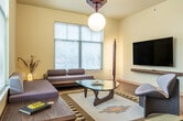 This thoughtfully designed single-floor residence offers 3 bedrooms and 2 bathrooms across a well-utilized footprint. The open-concept living, dining, and kitchen area forms the heart of the home, bathed in natural light from multiple large windows that frame outdoor views. The living room showcases a distinctive mid-century modern aesthetic, highlighted by a sculptural pendant light fixture and warm hardwood flooring. The adjacent dining area features an octagonal marble-top table beneath a sleek pendant light, surrounded by windows that create an airy, inviting atmosphere.

The kitchen is a functional standout, centered around a spacious island with a light countertop accented by a decorative tile border and seating for two. Stainless steel appliances, gray cabinetry, and a suite of pendant lights contribute to a clean, contemporary look. The primary bedroom offers a comfortable retreat with a walk-in closet, a ceiling light fixture with warm tones, and a bold geometric-patterned carpet. The additional bedrooms share a similarly cozy character with ample closet storage.

Both bathrooms mirror each other in layout, each featuring a tub-shower combination, a wide vanity with light wood cabinetry, and a large mirror. The hallways connect the spaces efficiently, completing a cohesive and well-appointed single-level home.
