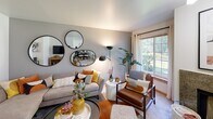 Located at 1296 NE Mount Olympus Lane in Bremerton, Washington, this single-floor residence offers a well-organized layout that balances comfort and functionality throughout. The living room serves as the heart of the home, highlighted by a striking granite-surround wood-burning fireplace and a sliding glass door that opens to a private patio overlooking lush greenery. Large windows flood the space with natural light, bringing the outdoors in. Adjacent to the living area, the dining space features its own window with garden views and ample room for a full dining set. The galley-style kitchen is fitted with light wood cabinetry, laminate countertops, and stainless steel appliances, including a range, microwave, and dishwasher, all set atop wood-look flooring. The primary bedroom offers plush carpeting, a spacious reach-in closet with sliding doors, and a serene, neutral color palette. A second bedroom also features carpeted floors and a generous closet. Two full bathrooms serve the residence, each with a tub-shower combination and wood-look flooring. One bathroom features warm wood-toned cabinetry with a large vanity mirror, while the other presents a clean, contemporary aesthetic with crisp white finishes. Throughout the home, soft neutral tones and natural light create a calm, inviting atmosphere.