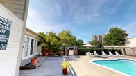 This single-storey property offers a well-appointed outdoor living area designed for relaxation and recreation. At the heart of the exterior is a swimming pool, accompanied by a spacious poured-concrete pool deck furnished with lounge chairs and a shaded umbrella seating area, ideal for unwinding on sunny days. Adjacent to the pool, a wooden deck extends from the main structure, adding warmth and a natural aesthetic to the outdoor space. The building itself features large French-style glass doors that open directly onto the deck, creating a seamless transition between indoor and outdoor living. Potted plants and container gardens are positioned throughout, lending greenery and character to the patio areas. A brick-pillar gated entrance leads to the property, framed by mature, leafy trees that provide privacy and shade. The surrounding landscape is lush, with well-established trees creating a green backdrop against an open sky. The overall ambiance is that of a serene, resort-like retreat, offering both functional amenities and a pleasant outdoor environment suited for leisure and entertaining.