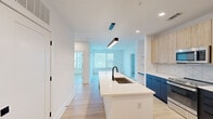 This thoughtfully designed 2-bedroom, 1-bathroom residence offers a clean, modern aesthetic across a single floor. The open-concept layout centers around a stunning kitchen featuring a large white quartz island with a matte black undermount sink, bold navy lower cabinets, light wood upper cabinetry, and a geometric tile backsplash. Stainless steel appliances, including a French door refrigerator, electric range, and built-in microwave, complete the kitchen. A sleek linear pendant light anchors the island, adding an architectural focal point. Light wood-tone flooring runs seamlessly throughout, enhancing the bright, airy atmosphere created by recessed lighting and abundant natural light from multiple windows. Open shelving in the living area provides both display and storage options. The two bedrooms are well-proportioned, with the primary bedroom offering a ceiling fan and generous window views. The second bedroom benefits from natural light and direct access to the main living area. The full bathroom is finished with crisp white subway tile in a walk-in glass shower, matte black fixtures, and wood-tone flooring. Two dedicated closets provide ample storage, rounding out this efficiently designed, contemporary residence.