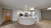 This single-floor residence offers a thoughtfully designed open-concept layout that seamlessly connects the kitchen and living areas. The kitchen is a standout feature, anchored by a distinctive curved peninsula topped with granite countertops and an integrated sink. White shaker-style cabinetry lines the walls, complemented by a full suite of stainless steel appliances including a refrigerator, electric range, and over-the-range microwave. The flooring transitions from tile in the kitchen to plush neutral carpet throughout the living and bedroom areas, creating a warm and cohesive feel.

The living area is generously proportioned, featuring neutral taupe walls, recessed lighting, and sliding glass doors that invite natural light. The bedroom is comfortably sized with a ceiling fan, corner windows that allow ample sunlight, and soft carpeting. The bathroom is finished with white tile in a classic black-and-white checkerboard border accent, a full soaking tub with shower, white cabinetry, and a granite-topped vanity with a wide mirror.

A dedicated in-unit laundry closet houses a full-size washer and dryer, adding everyday convenience. The overall design is clean, neutral, and functional, providing a practical and comfortable living environment throughout.